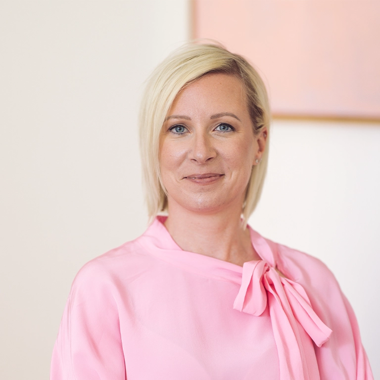 Portrait of a smiling blonde woman in a pink blouse with a bow, facing the camera.